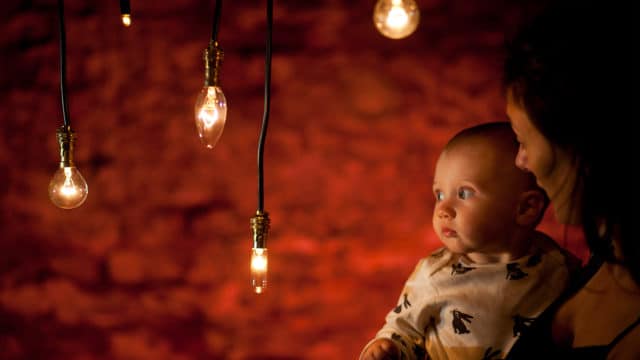 Mother holding a baby who is captivated by a lightbulb hanging on a wire.