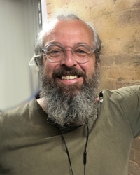 A headshot of a man with a grey beard wearing round glasses.