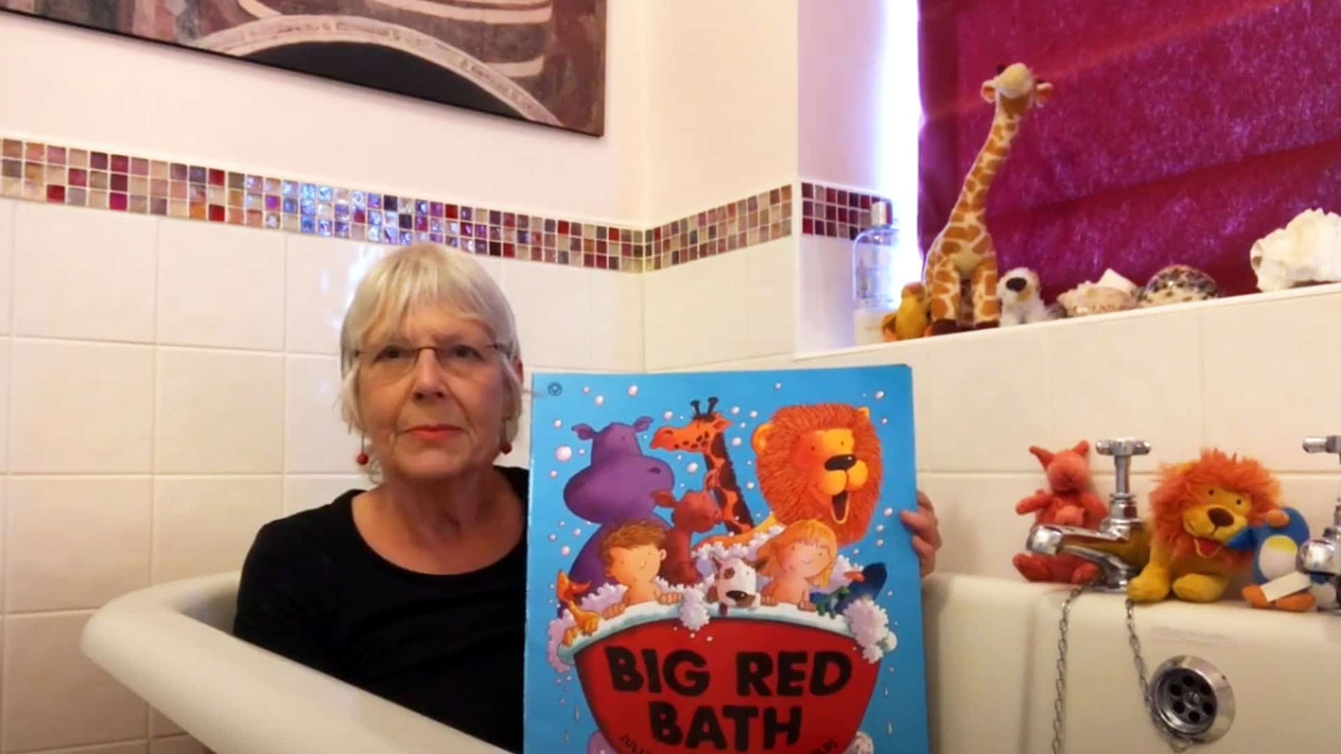 Author Julia Jarman sitting in the bath with her book, the Big Red Bath, surrounded by toys