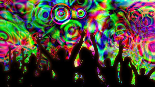 The silhouettes of people dancing with their hands in the air against a colourful kaleidoscopic background.